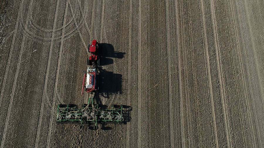 Top-down view of a field being traversed by a red and green seeder machine