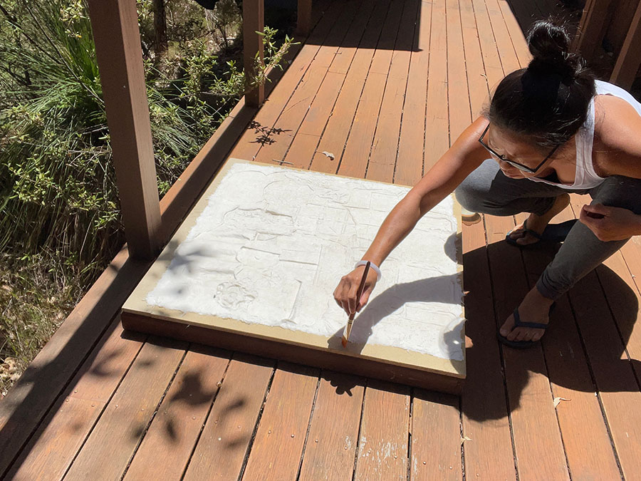 Jacky uses a small paint brush to wet the edges of a paper cast, roughly 1 metre by 1 meter, left to dry outside in the sun