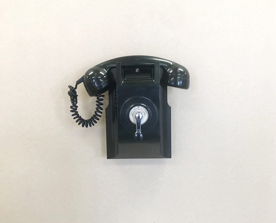 A black, rotary phone hanging from a wall